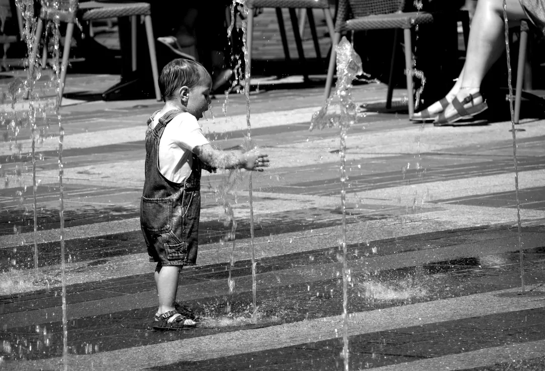 We zien een peuter met water spelen bij een fontein op straat.