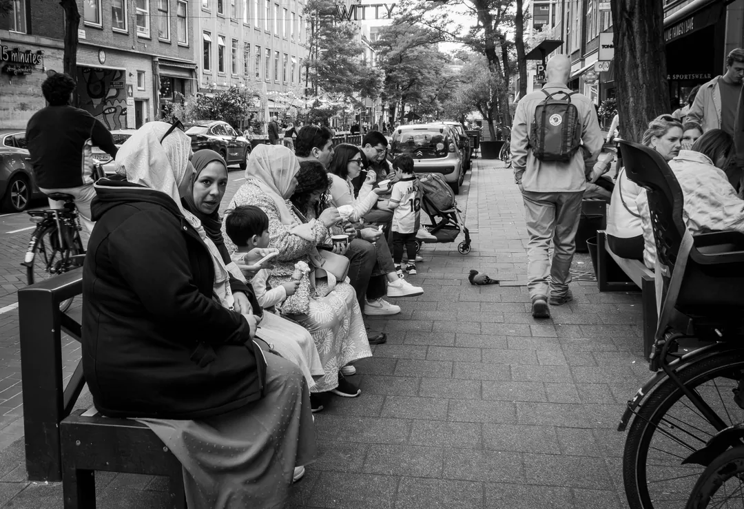 We zien hier een aantal dames en heren die genieten van een ijsje bij een ijssalon, maar in het midden heeft de duif het blijkbaar minder naar zijn zin...